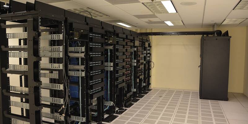 Rows of black server racks with blue network cables in a data centre with a raised tiled floor