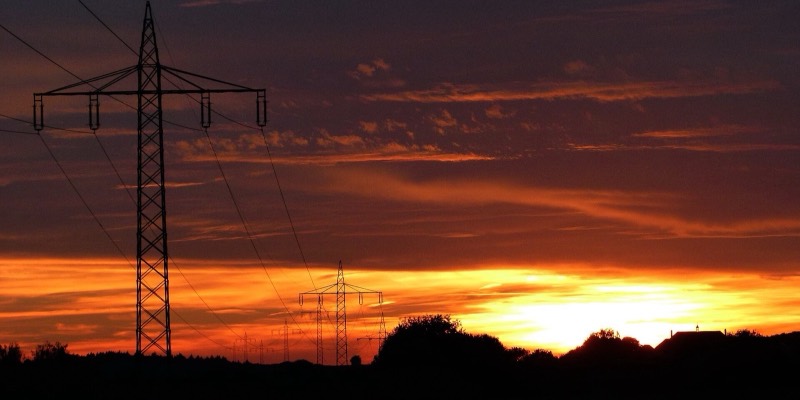 A high-voltage electricity pylon silhouetted against a red sunset