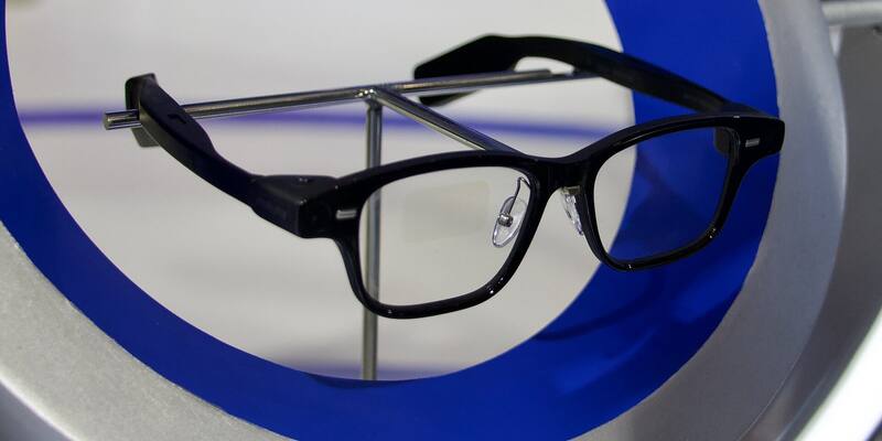 A pair of black-framed Alibaba Quark AI glasses on a metal display stand, framed by a blue and silver ring