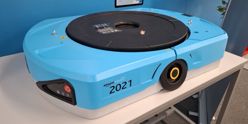A large, flat, light-blue Amazon Robotics drive unit robot with a black circular lifting plate on top, displayed on a white table