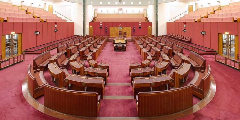 The empty Australian Senate chamber, with curved rows of red leather benches and wooden desks facing the President’s chair