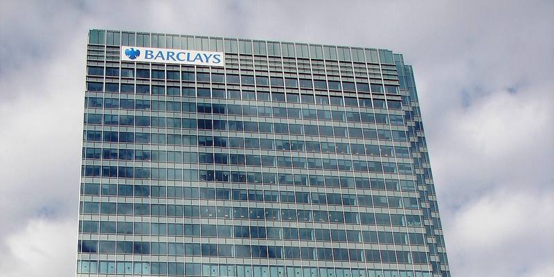 A tall glass office tower with a blue Barclays eagle logo and name near the top, against a cloudy sky