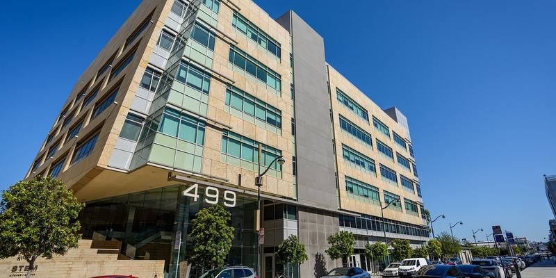 A six-storey stone and glass office building with a large 499 sign above its entrance, cars parked along the street under a clear blue sky.
