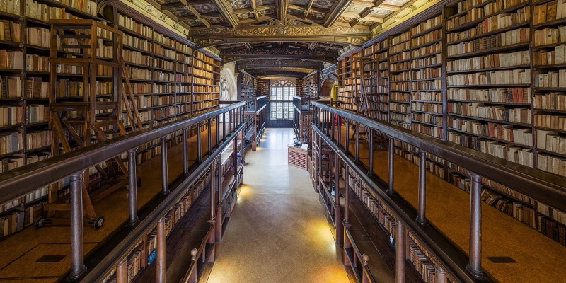 The interior of Duke Humfrey’s Library at the Bodleian, with tall wooden shelves of old books, a gallery railing and a painted ceiling