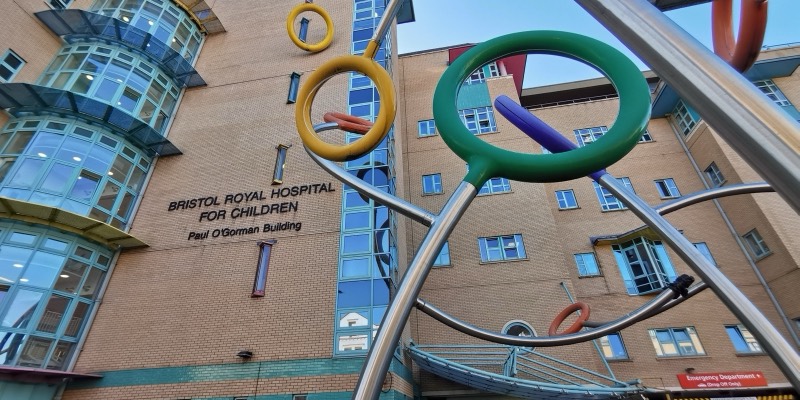 The Bristol Royal Hospital for Children building, with its name on the brick wall and a colourful ring sculpture in front