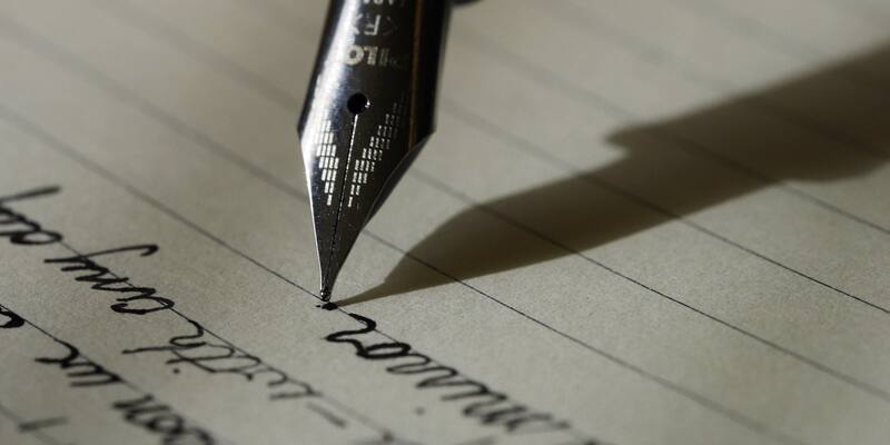 Close-up of a silver fountain pen nib resting on lined paper, with lines of handwriting below it and the pen’s shadow falling to the right