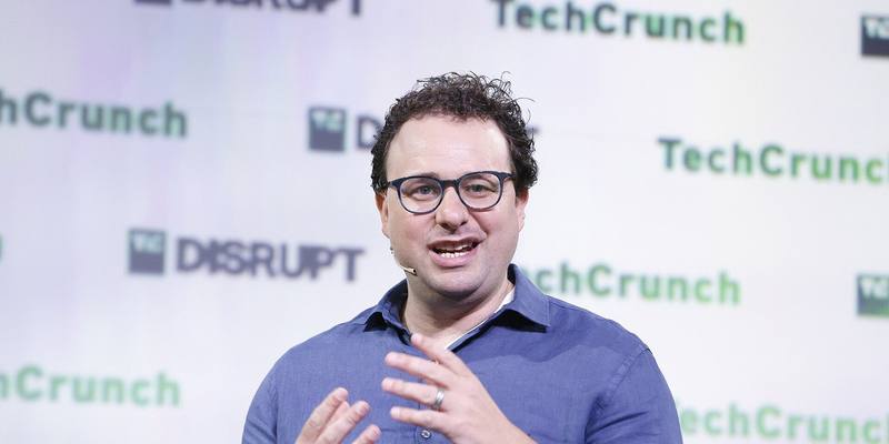 Dario Amodei, in glasses and a blue shirt, gesturing as he speaks on stage in front of a TechCrunch Disrupt backdrop