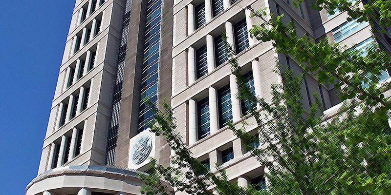 The tall pale stone tower of the Thomas F. Eagleton US Courthouse against a blue sky, with a court seal on its facade and green trees in front.