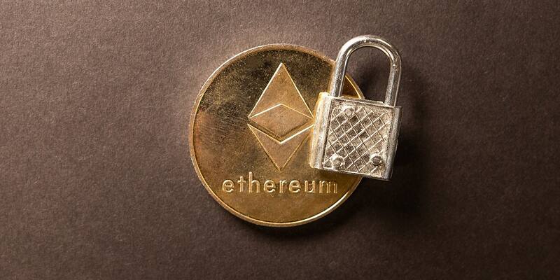 A gold Ethereum coin with a small silver padlock resting on it against a dark brown background.