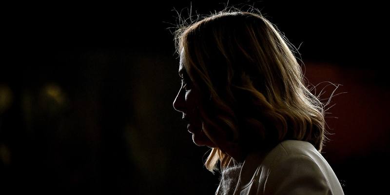 Giorgia Meloni in side profile, her face and hair lit from behind against a dark background