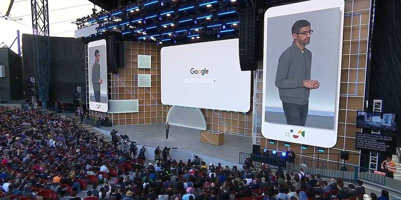 A large crowd watches Sundar Pichai on an outdoor stage, with his image on two tall screens either side of a big Google search screen