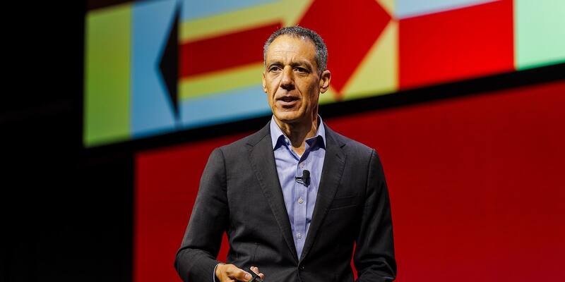 Hany Farid, in a dark jacket and blue shirt, speaks on a stage in front of a large red and multicoloured screen