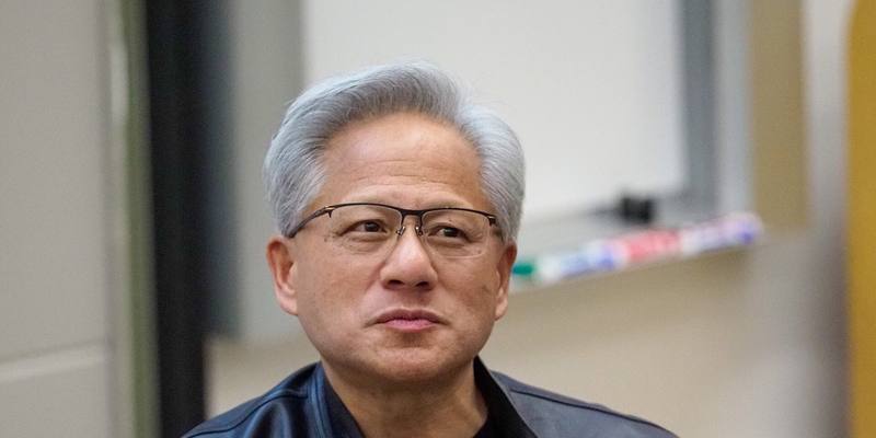 Close-up of Jensen Huang, with grey hair and rimless glasses, wearing a black leather jacket in a classroom