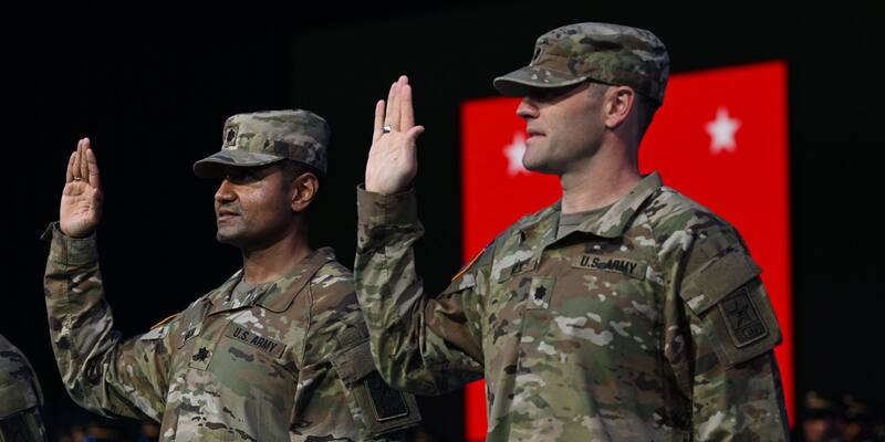 Kevin Weil and Shyam Sankar in US Army uniforms raising their right hands to take the oath of office in front of a red flag