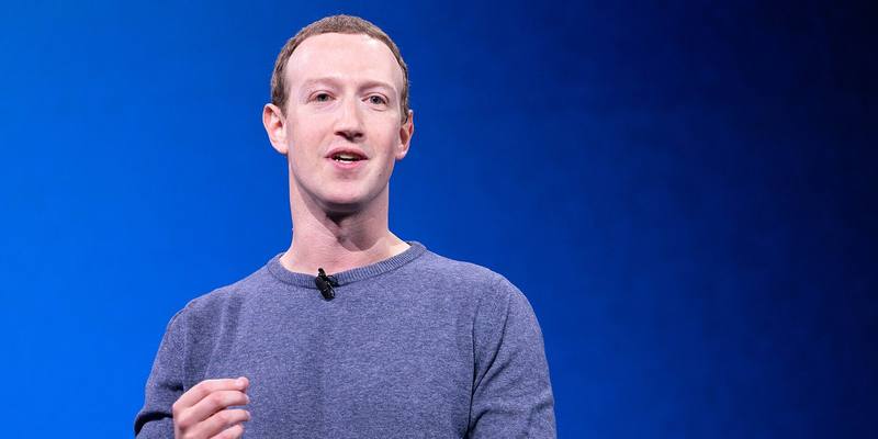 Mark Zuckerberg in a grey jumper speaking on stage in front of a blue backdrop