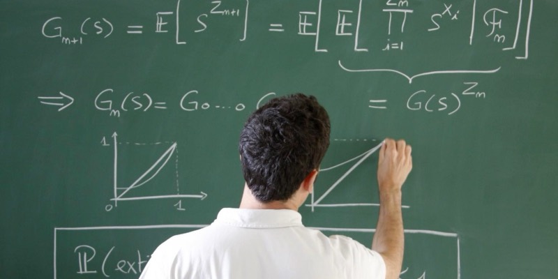 A mathematician writing equations and graphs on a green chalkboard