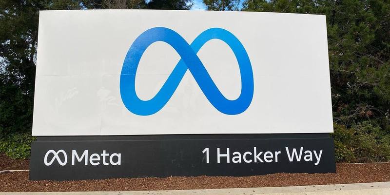 A large white sign with Meta's blue infinity logo on a black base reading Meta and 1 Hacker Way, in front of trees