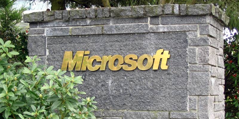 Gold Microsoft lettering on a grey granite sign post, with green shrubs in front