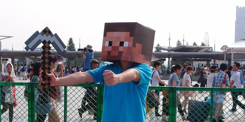A person wearing a blocky Minecraft Steve head and holding a cardboard pickaxe outside a convention centre