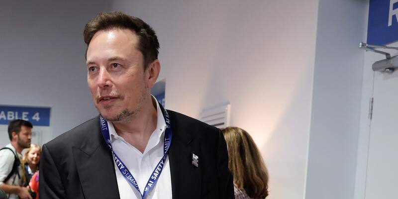 Elon Musk in a dark suit and an AI Safety Summit lanyard, looking to one side