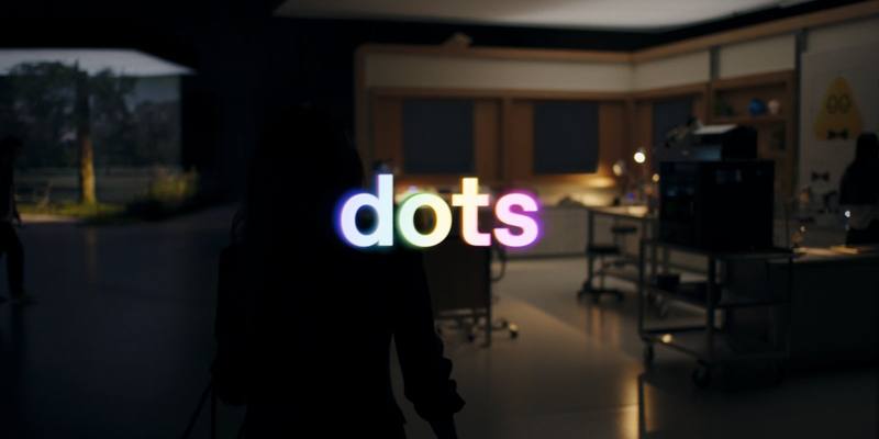The word dots glowing in rainbow colours over a dim studio, with a figure in silhouette in the foreground