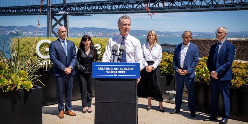 Gavin Newsom speaking at a lectern with a sign reading Creating an AI-ready workforce, with five people standing behind him and the Bay Bridge in the background