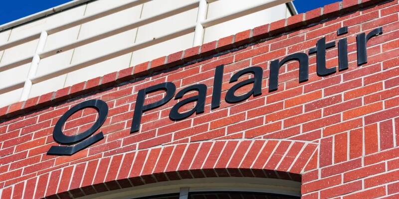 Black Palantir logo and lettering on a red brick office wall against a blue sky