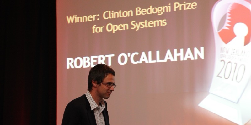 Robert O’Callahan walks across a stage in front of a large screen reading “Winner: Clinton Bedogni Prize for Open Systems, Robert O’Callahan”