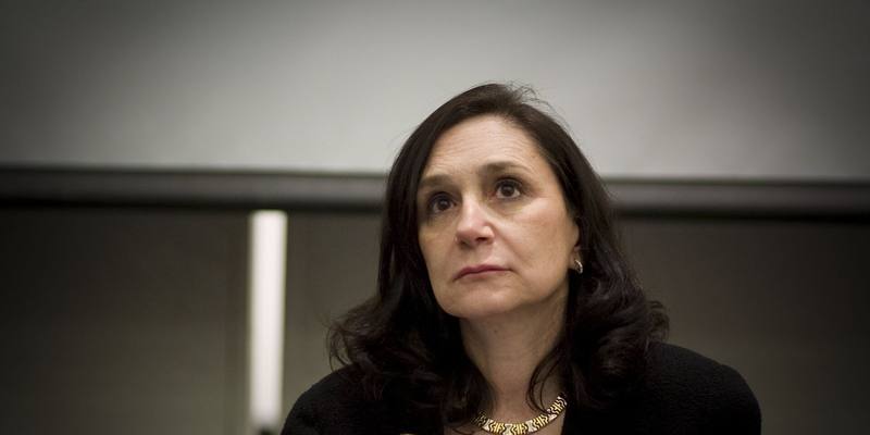 Sherry Turkle, with shoulder-length dark hair and a black jacket with a gold flower brooch, looking upwards thoughtfully