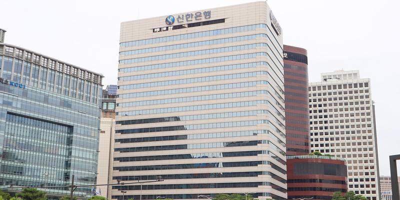 A tall cream-coloured office tower with the Shinhan Bank logo and Korean lettering at the top, beside other office buildings in Seoul