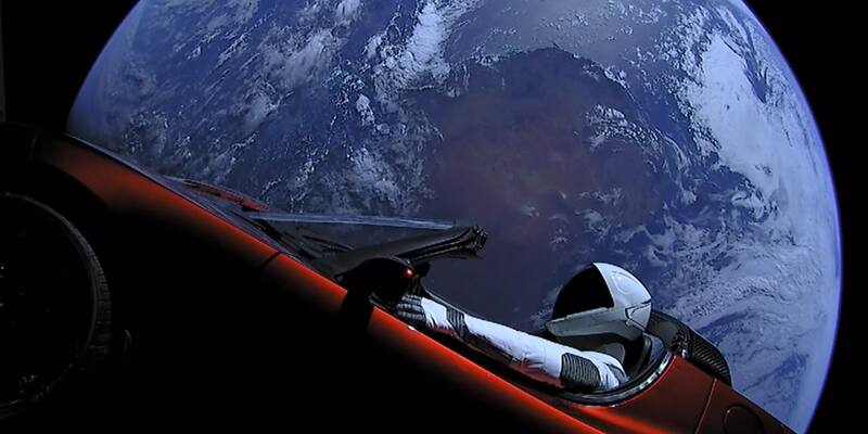 A red Tesla Roadster with a mannequin in a white SpaceX spacesuit in the driver’s seat, floating in space with Earth behind it
