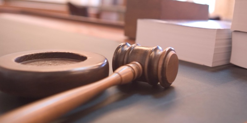 A wooden judge’s gavel resting beside its sound block on a courtroom desk, with thick legal books behind