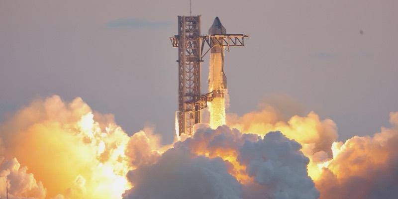 SpaceX's Starship rocket lifting off beside its launch tower, surrounded by huge orange-lit clouds of exhaust at sunrise