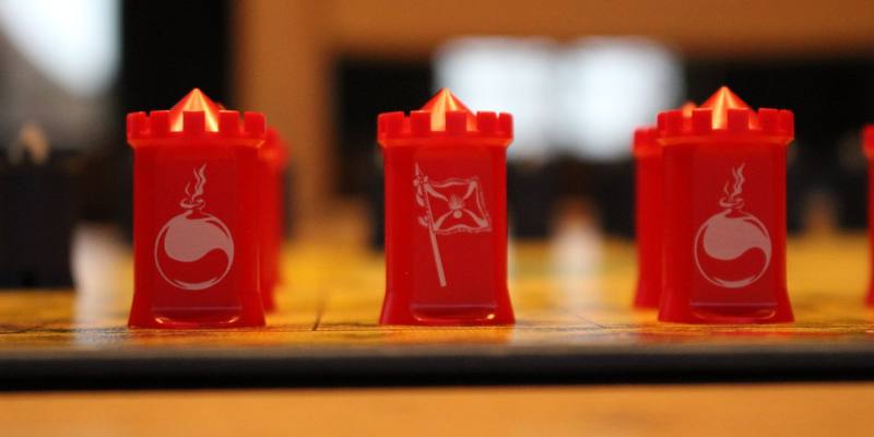 Three red Stratego pieces on a board, showing a bomb, a flag and another bomb