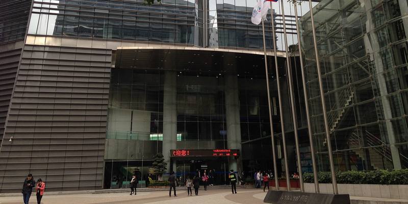 Glass-fronted entrance of Tencent’s headquarters in Shenzhen with flagpoles and a Tencent name sign in the foreground