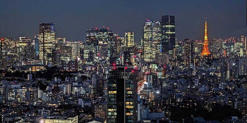 Lit office towers of Roppongi and the orange Tokyo Tower against a dark blue night sky, above a dense spread of city lights