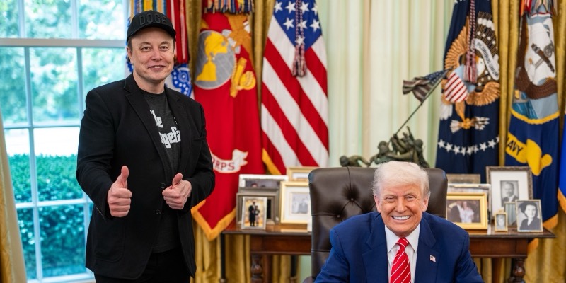 Elon Musk, in a black DOGE cap, gives two thumbs up beside a smiling Donald Trump seated at the Resolute Desk in the Oval Office
