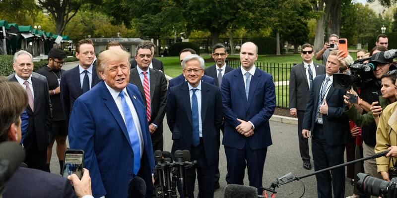 Donald Trump in a blue suit talking to reporters holding microphones and cameras outside the West Wing, with Jensen Huang and other tech executives standing behind him