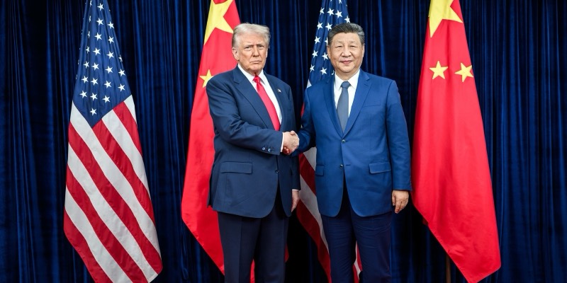 Donald Trump and Xi Jinping shake hands in front of US and Chinese flags and a dark blue curtain