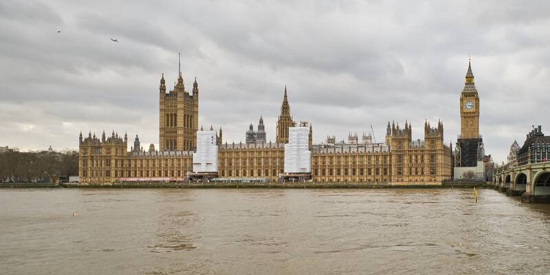 The Houses of Parliament and the Elizabeth Tower (Big Ben) beside the River Thames under a grey sky, with Westminster Bridge on the right