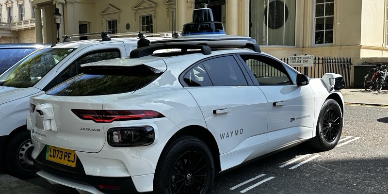 A white Waymo-branded Jaguar I-Pace with a roof-mounted sensor dome, parked on Carlton House Terrace SW1 in London with a UK number plate