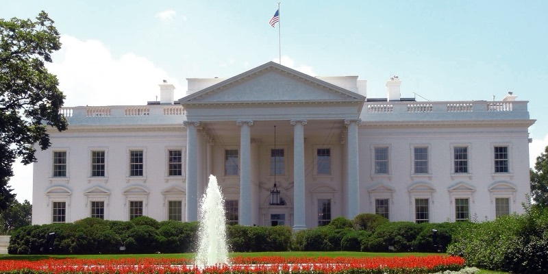 The White House north facade with its columned portico, a fountain and red flower beds on the lawn in front